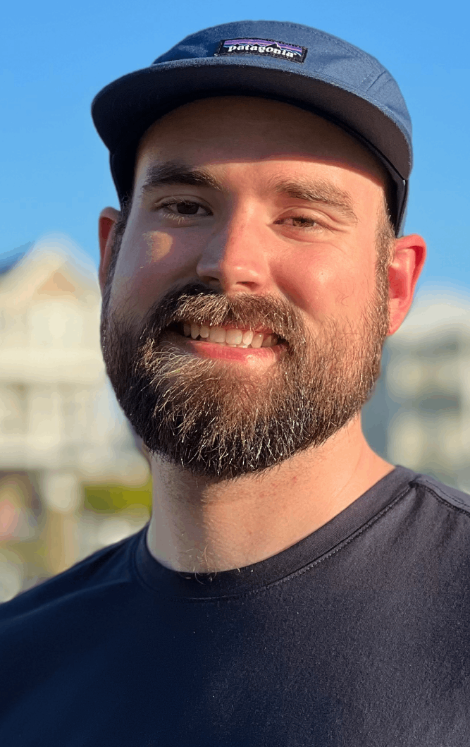 A photograph of lighting designer Daniel Shiels, outdoors and smiling, wearing a blue Patagonia cap and a black t-shirt.